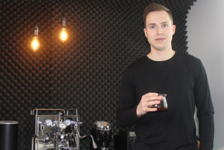 Man holding coffee cup in front of espresso machine with slight smile.