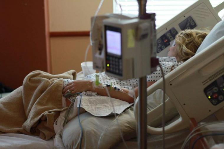 Image of shallow focus on patient in hospital bed behind monitor and IV supplier