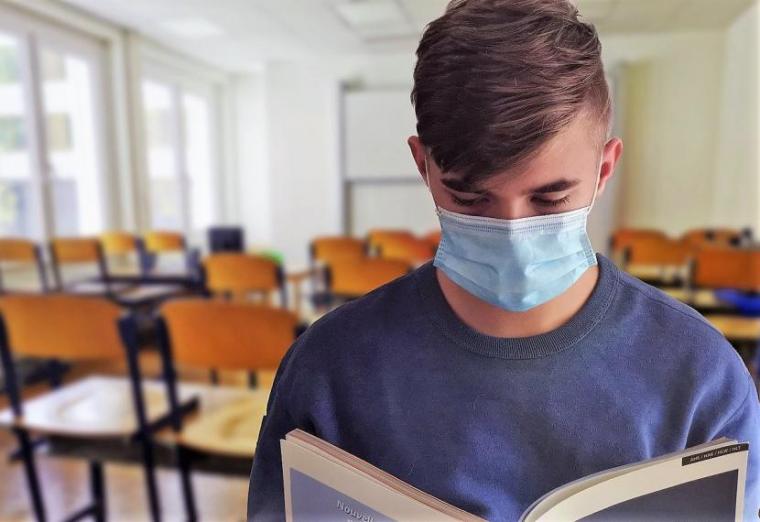 Student wearing mask looking at book with classroom in background