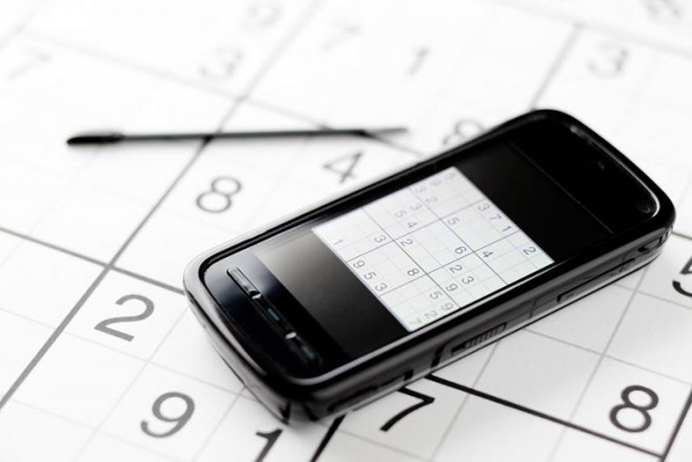 iPhone sitting on sudoku puzzle with pen in background
