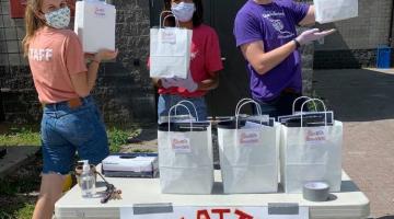 Staff standing behind Creative Encounters pickup table holding camp kit bags