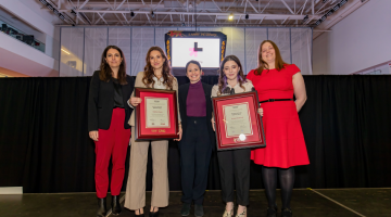 Five women stand on stage presenting awards smiling to camera