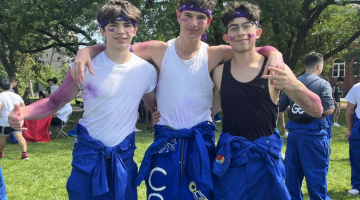 Three male students standing together outside at event, smiling to camera