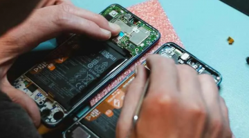 A pair of hands works on repairing the inside wiring of a phone laying on a table