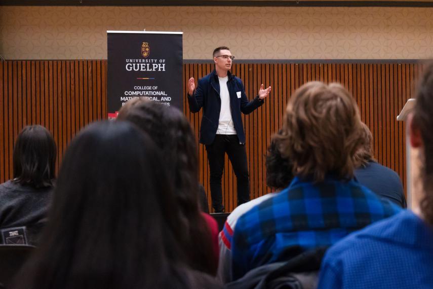 Audience members look on at Scott Sammons who stands on stage and animately presents