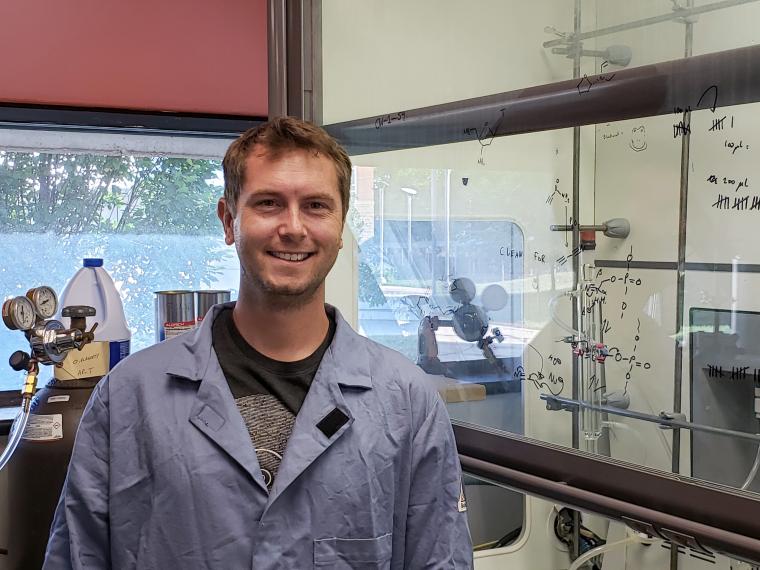 Prof. O'Flaherty stands next to a fume hood in a blue lab coat.