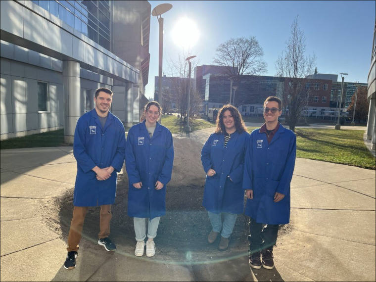 The 4 recipients of the first-year TAs Recognition Awards stand outside the SSC in blue lab coats.