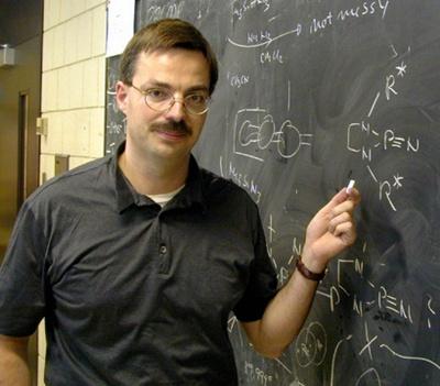 Prof Denk points to a molecule on a blackboard