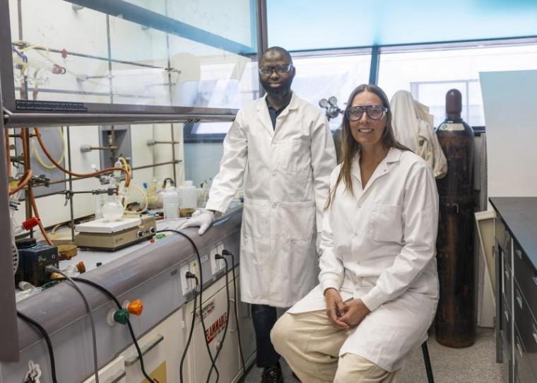 Dr. Kathryn E. Preuss and Mukaila A. Ibrahim in a lab beside lab equipment. 