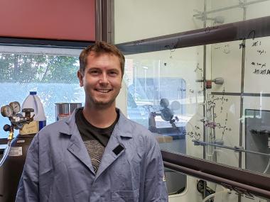 Prof. O'Flaherty stands next to a fume hood in a blue lab coat.