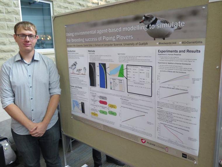 A computing student stands in front of a research poster