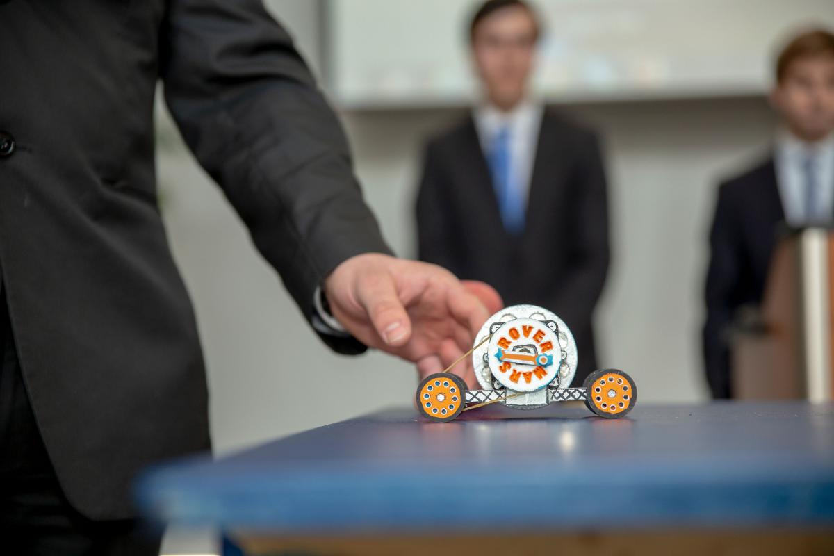 student hand reaching toward a small 3D-printed toy car