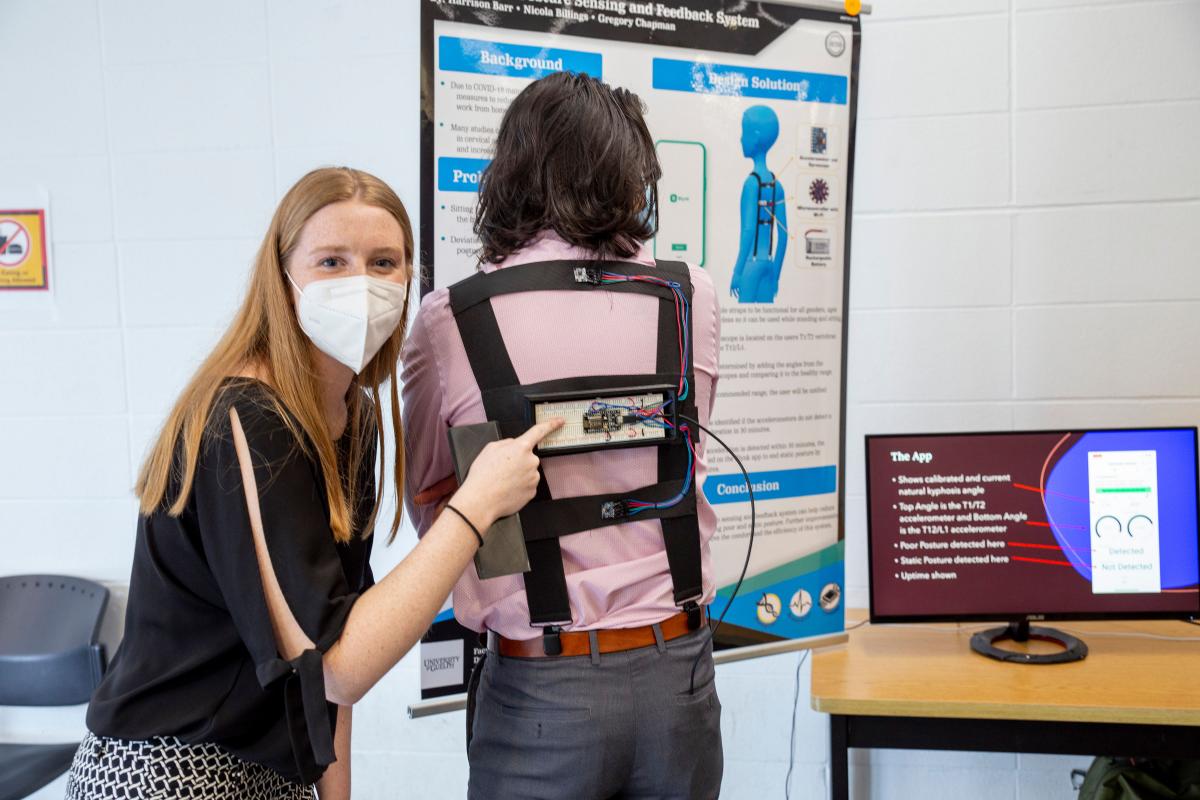 a student pointing to a device located on another student's back