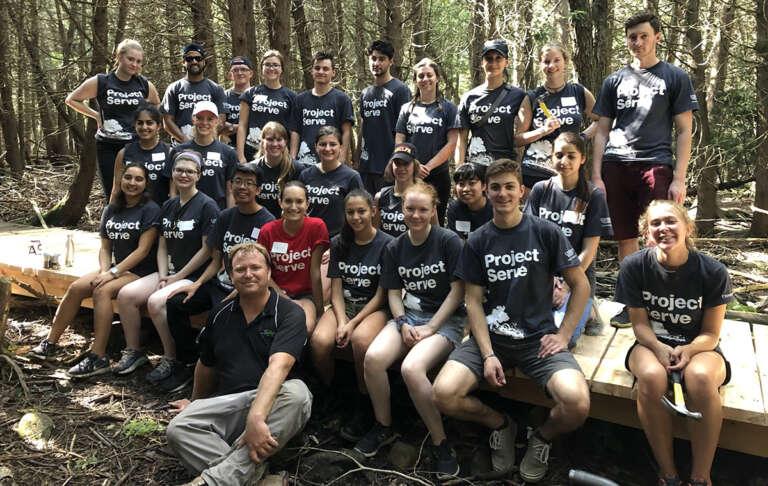 Dave Beaton sits with the Project Serve team that helped repair boardwalks along the Hanlon Creek trail in 2019