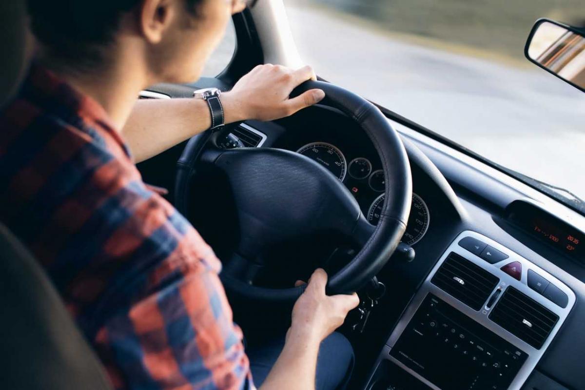 Male driving a car, gripping the steering wheel with both hands