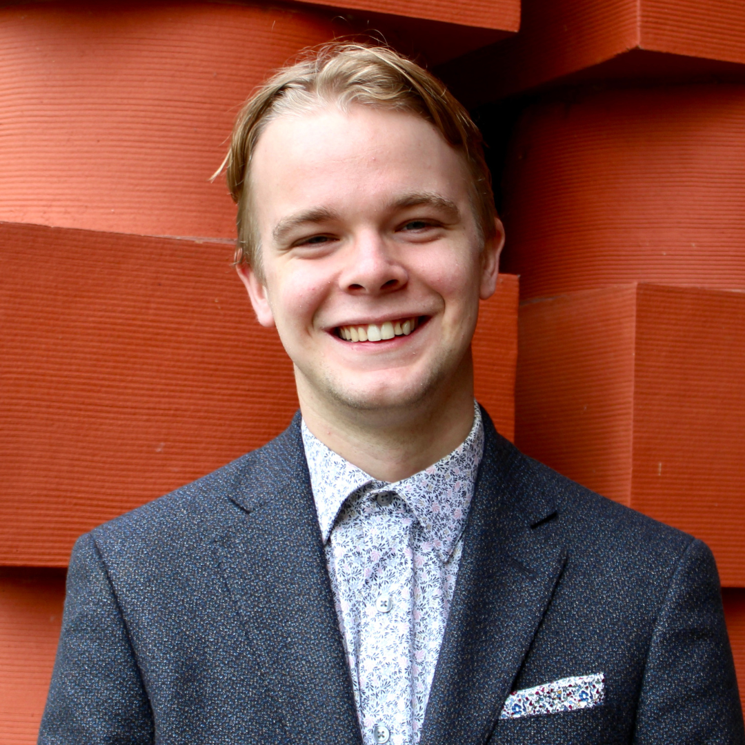 male student outdoors with bulding and bushes faded in the background