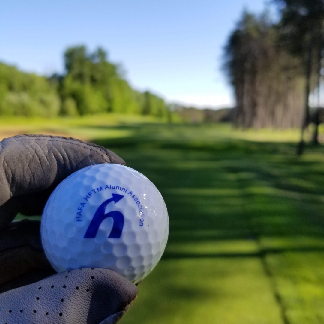 Someone holding a golf ball with the association logo on it