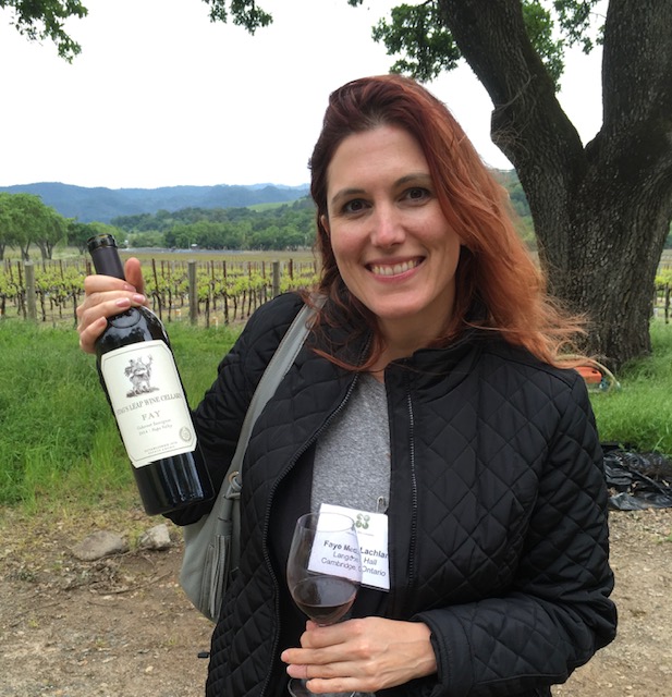 photo of a person holding a bottle of wine and glass of wine with a vineyard backdrop