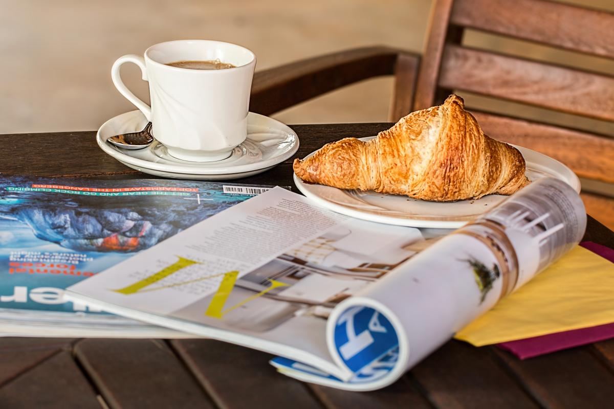 Photo of coffee cup, croissant and newspaper