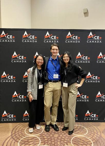 Three students standing in front of a competition back drop