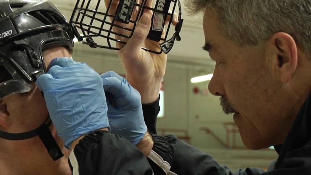 Dr. Lawrence Spriet helping a hockey player with his helmet