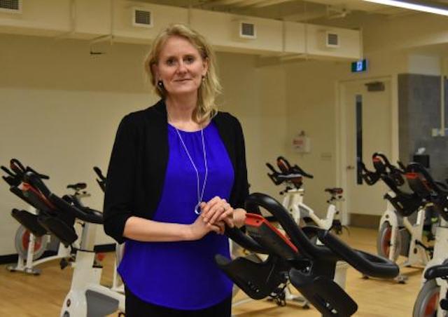 A photograph of Dr. Lori Vallis of the research team posing with exercise bikes.