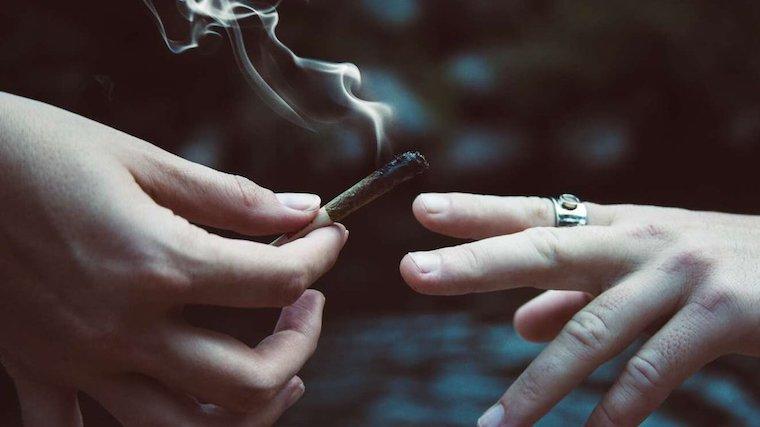 A photo of one hand passing a lit cannabis cigarette to another hand.