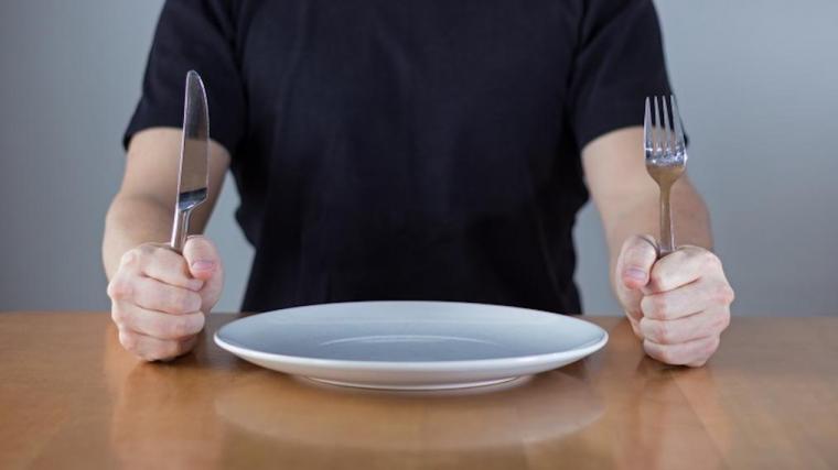 A photograph of a man with and empty plate and a knife and fork