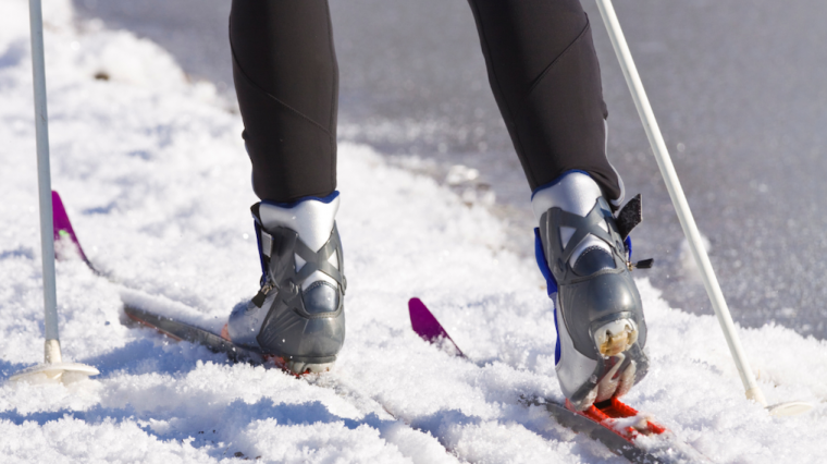 A cross-country skier, shown from the knees down, skiing on snow.