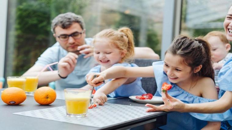 A photograph of pre-schoolers eating strawberries and drinking orange juice with an adult.