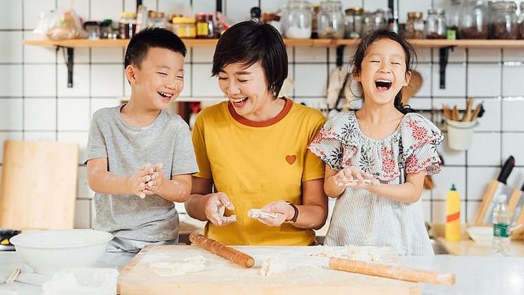 A photograph of a mother and children laughing and baking bread together