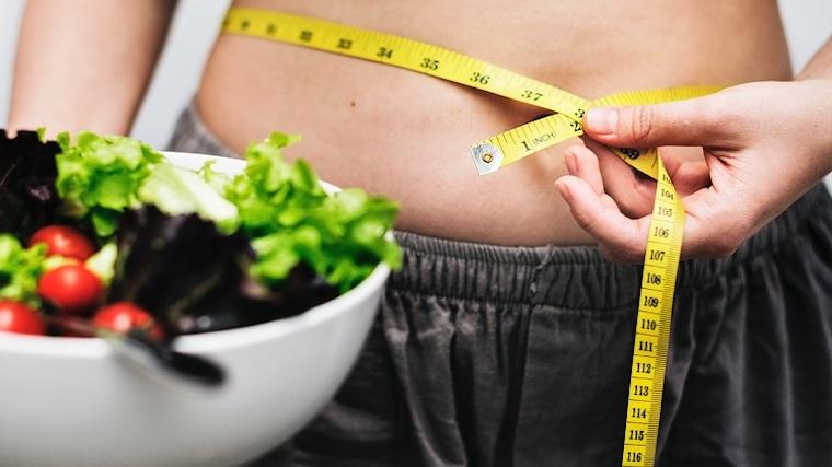 A photograph of a bowl of salad and a woman measuring her belly