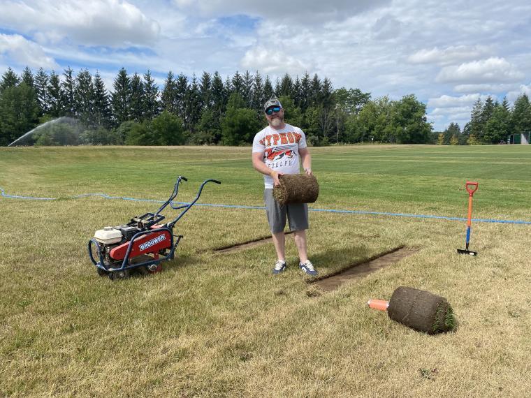 Cam Shaw holding a roll of sod in a field of grass