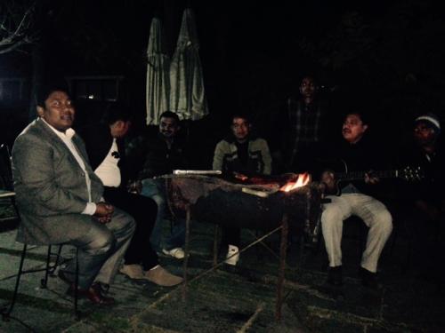 men sitting in chairs around a fire, singing