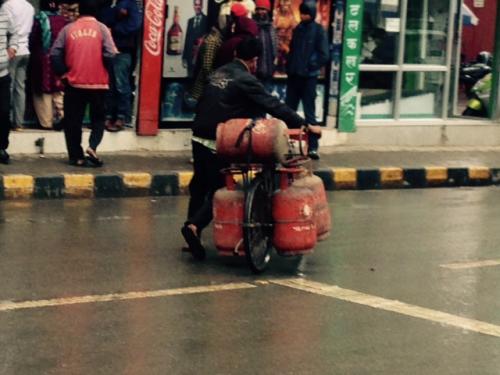 Man on a crowded street with a bicycle loaded with propane tanks