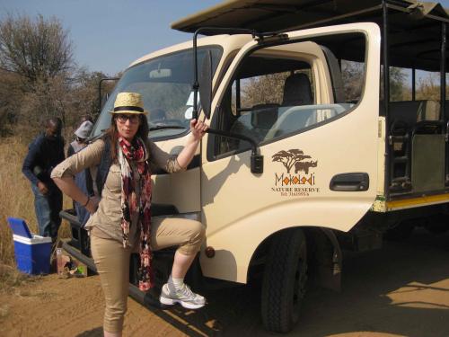 Stephanie in safari clothing holds onto front door of a safari truck with Mokolodi truck