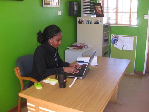 Dionne sits at a desk working at at computer, green wall behind her