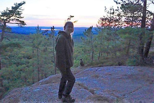 Dr. Leslie Rye standing on a cliff overlooking Algonquin Park at sunset