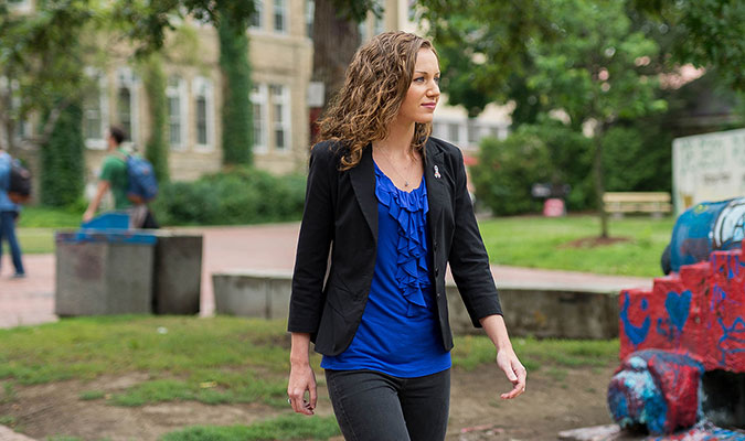 A woman shows her walking through U of G campus, with students and the canon out-of-focus in the background.