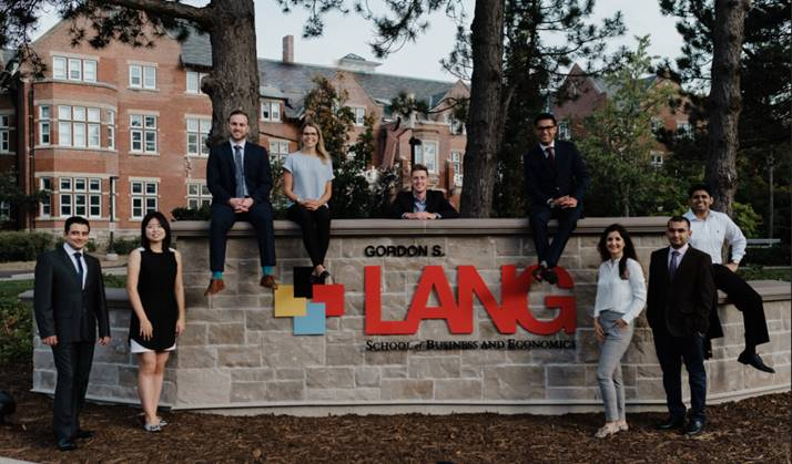 Students standing beside the Lang School logo