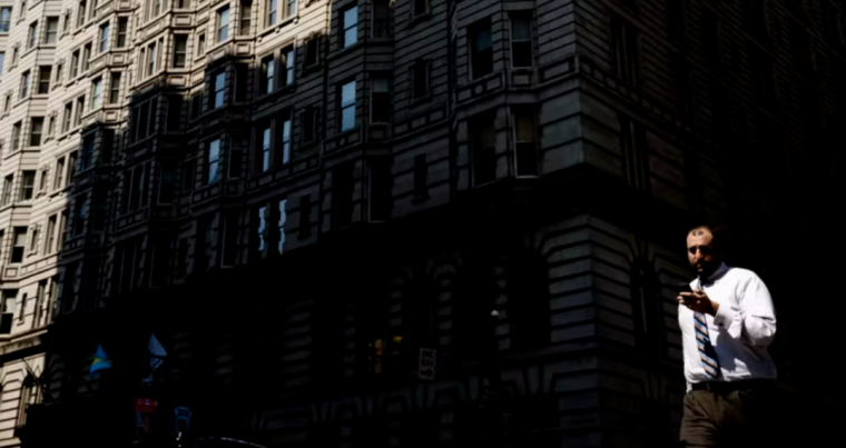 A pedestrian views his smartphone as he crosses a city street.