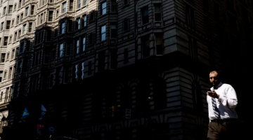 A pedestrian views his smartphone as he crosses a city street.