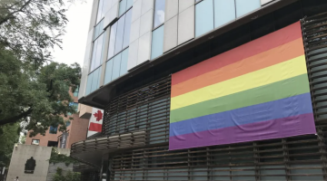 Pride flag hanging on a building with a Canadian flag in the background, less prominent.