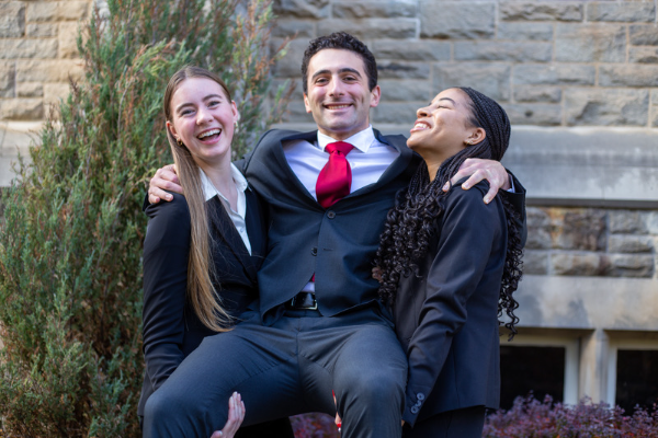 Two commerce students holding a third student laughing