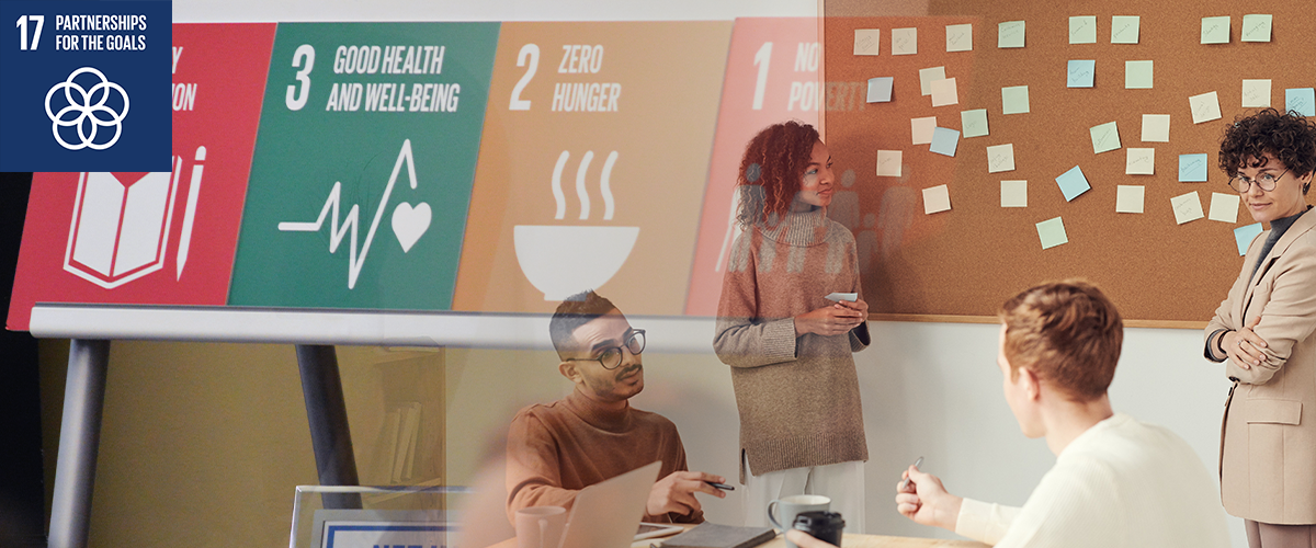 Photo of students collaborating, with an image of Sustainable Development Goals written on tiles in the background