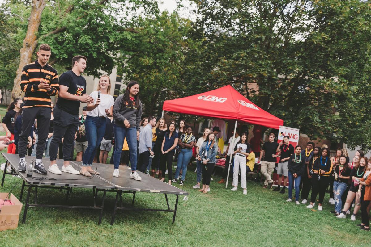 Katelyn Cortina on a stage with her LSA teammates at an outdoor event speaking to students.