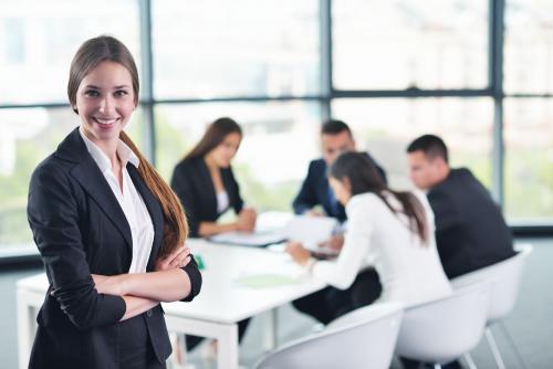 Girl in business group standing with arms crossed with group of colleagues meeting in the background