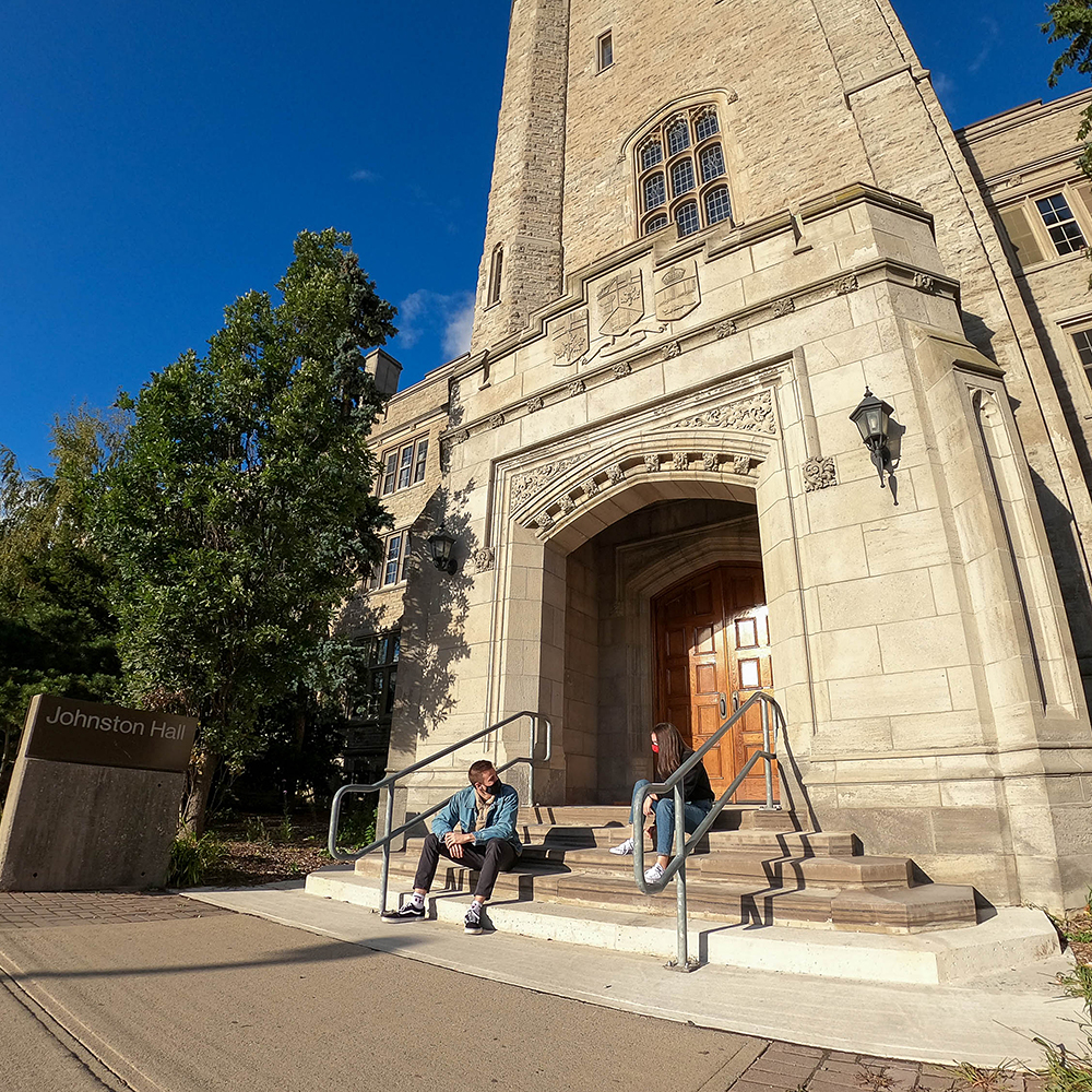 students in masks sitting on the front steps of Johnston Hall