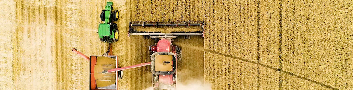 A red combine harvesting wheat going into a trailer pulled by a green tractor.