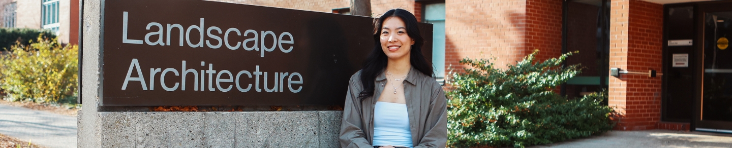 Catherine Yan smiling for the camera while sitting next to the Landscape Architecture building sign.